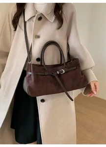 Détail d'un sac cabas en daim marron foncé avec boucles argentées et lanières sur manteau