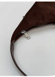 Detail of silver zipper and dark leather strap on a brown suede hobo bag