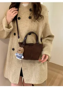 Detail of dark brown suede bucket bag featuring a cute plush bear charm on white coat