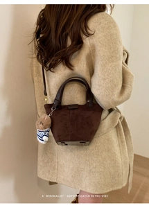 Detail of dark brown frosted suede bucket bag with bear charm on a beige coat