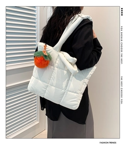 Detail der weißen gesteppten Nylon-Tragetasche mit kreativem orangefarbenem Plüsch-Anhänger
