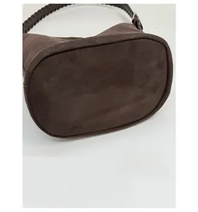Detailed view of the wide oval base and woven handle on a dark brown suede bucket bag