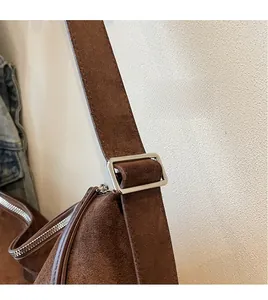 Detail van bruine suède draagtas met brede verstelbare riem en zilveren metalen gesp