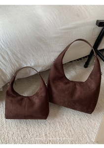 Detail view of two dark brown suede tote bags with retro stitching on white bedding