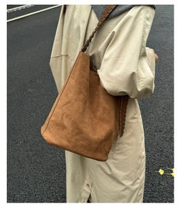 Détail d'un sac seau en daim marron foncé avec bandoulière tressée dans un décor d'automne