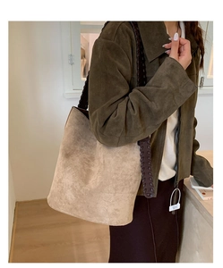 Détail d'un sac seau en daim beige avec bandoulière tressée marron sur une veste en cuir olive