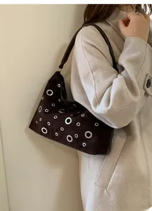 Detail of dark brown suede shoulder bag featuring silver metal eyelet grommet accents