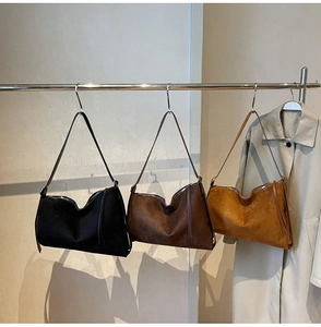 Drie minimalistische suède hobo-tassen in zwart en bruin hangend aan een metalen rek