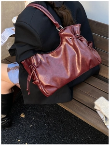 Detail of burgundy PU leather tote bag with drawstring and side pocket in urban setting