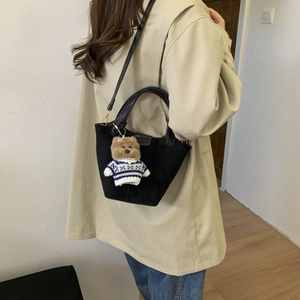 Detail of black suede-textured bucket bag with crossbody strap and cute teddy bear charm