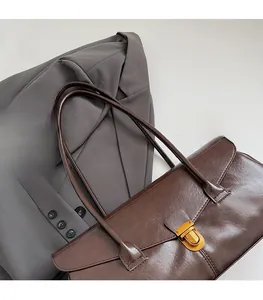 Detail of a dark brown tote bag with a gold turn-lock over a grey blazer and book