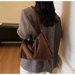 Detail of dark brown suede shoulder bag with tassel and slouchy crescent shape on model