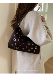 Detail of dark brown suede crescent bag with silver eyelets worn on the shoulder