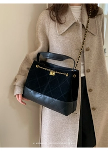 Detail of black quilted bucket bag with gold chain strap shown on beige coat outfit