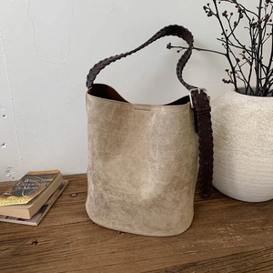 Detail of vintage khaki suede bucket bag featuring a dark brown braided leather strap