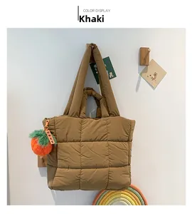 Detailansicht der khakifarbenen Stepptasche mit Plüschanhänger an einem Holzhaken