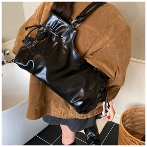Detail of black oiled leather tote bag with drawstring closure and glossy wrinkled texture