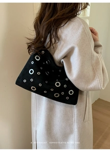 Detail of retro black suede shoulder bag with silver eyelets on a beige coat