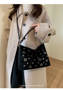 Close-up of minimalist black suede shoulder bag with silver eyelet details on a model