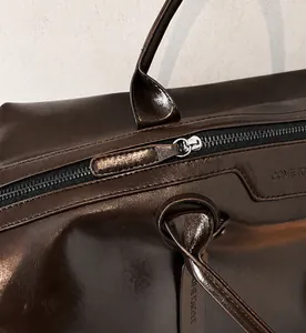 Dettaglio della cerniera argento e trama in pelle marrone lucida della borsa tote