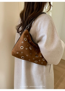 Close-up of brown suede shoulder bag featuring silver metal grommets and retro design