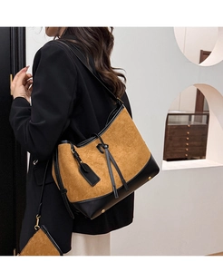 Detail of suede bucket bag with leather trim and metal feet on a black blazer