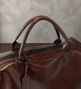 Dettaglio dei manici imbottiti e della texture in pelle di una borsa da viaggio marrone