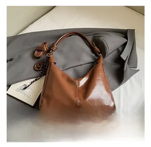 Detail of a brown leather shoulder bag featuring knotted handles and metal ring pendant