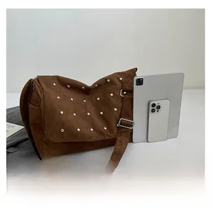 Sac bandoulière en daim marron avec rivets argentés comparé à une tablette tactile