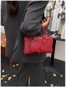 Red leather handbag with a round coin pouch and metallic studs shown in a street style shot