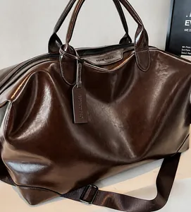 Dettagli della borsa da viaggio marrone scuro lucida con logo e tracolla larga