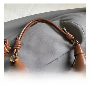 Detail of a brown glossy leather handbag featuring unique knotted handles and gold hardware
