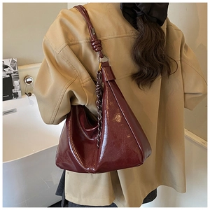 Detail of burgundy glossy patent leather underarm bag with unique knotted strap and woven charm