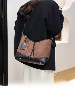 Détail du sac patchwork en daim et cuir avec pieds en métal doré et accessoire suspendu