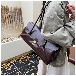 Close-up of a large brown vintage tote bag with a golden buckle closure on a shoulder strap