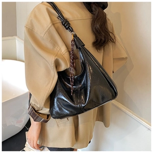 Detail of glossy black hobo shoulder bag with knot strap and woven tassel charm