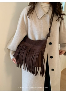Detail of dark brown faux suede crossbody bag with retro fringes worn over a beige coat