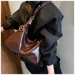 Détail du sac sous le bras marron foncé brillant montrant la sangle à nœud sur l'épaule