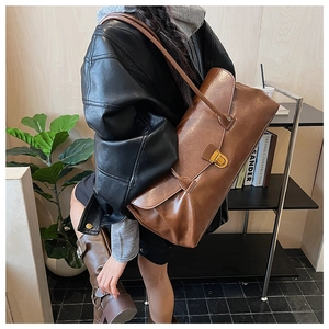 Detail of a brown leather tote with golden metallic buckle worn by a model in casual setting