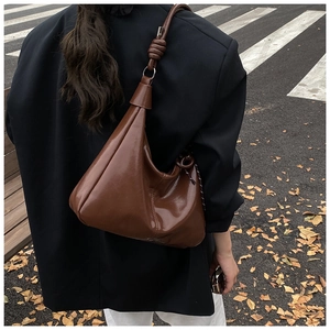 Detail of dark brown glossy leather shoulder bag with unique knotted strap and silver ring