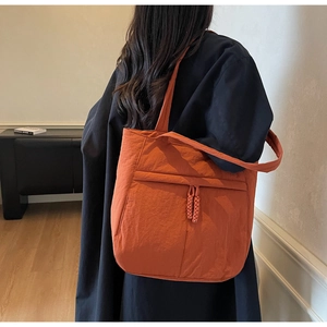 Detail der orangefarbenen Nylon-Tragetasche mit Faltenstoff und Vordertasche an der Schulter