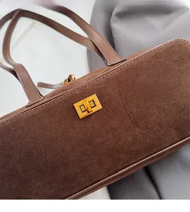 Detailed macro view of soft brown suede fabric and gold metal twist lock on baguette bag