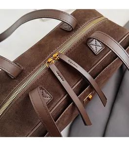 Detail view of smooth dual golden zippers on dark brown suede baguette bag surface
