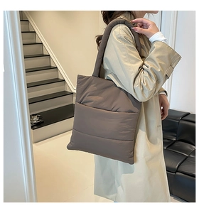 Brown quilted puffer tote bag with wide shoulder strap worn by a model in interior setting