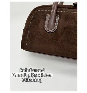 Detail of dark brown suede bag featuring reinforced handles and precision white stitching