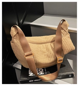 Dettaglio borsa hobo beige trapuntata con trama ondulata e tracolla regolabile su un libro