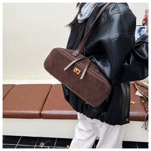 Detail of dark brown suede baguette bag featuring a gold clasp and a long leather tassel