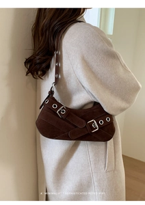Detail of retro brown suede baguette bag with metal buckle straps on light wool coat