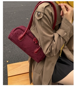 Detail of burgundy Boston bag with suede finish worn by model on a wooden bench