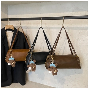 Detailed view of three cylindrical crossbody bags in brown and black with bear charms